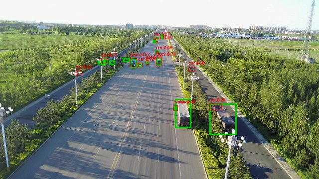 Aerial view of a wide road with trees. Two large trucks in the foreground have green ground-truth boxes, but the red predictions cover only small parts of them and label one as a car.